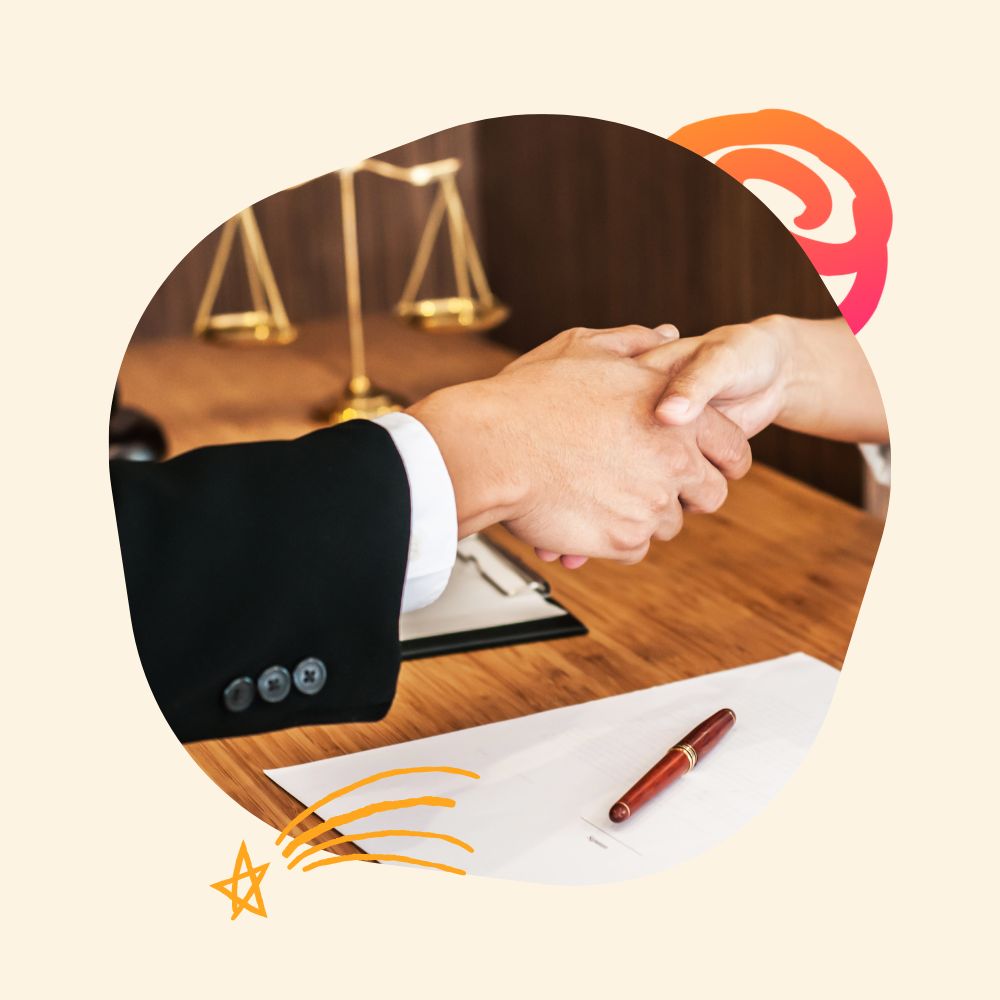 Two people shaking hands over a desk with a contract and pen in the foreground. The background includes a set of brass scales, symbolizing law or justice.