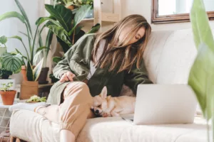 Woman falling asleep on her couch with her dog, while working from home next to her laptop computer.
