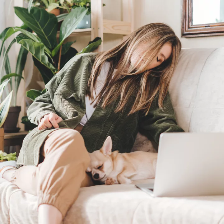 Woman falling asleep on her couch with her dog, while working from home next to her laptop computer.
