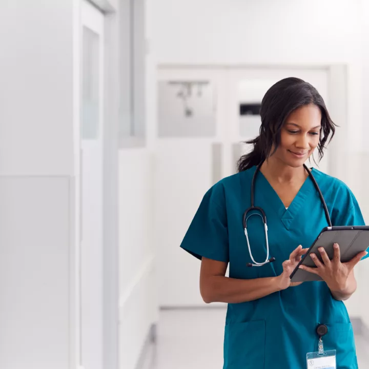 Female doctor wearing scrubs in hospital corridor using digital tablet working an in-demand healthcare job