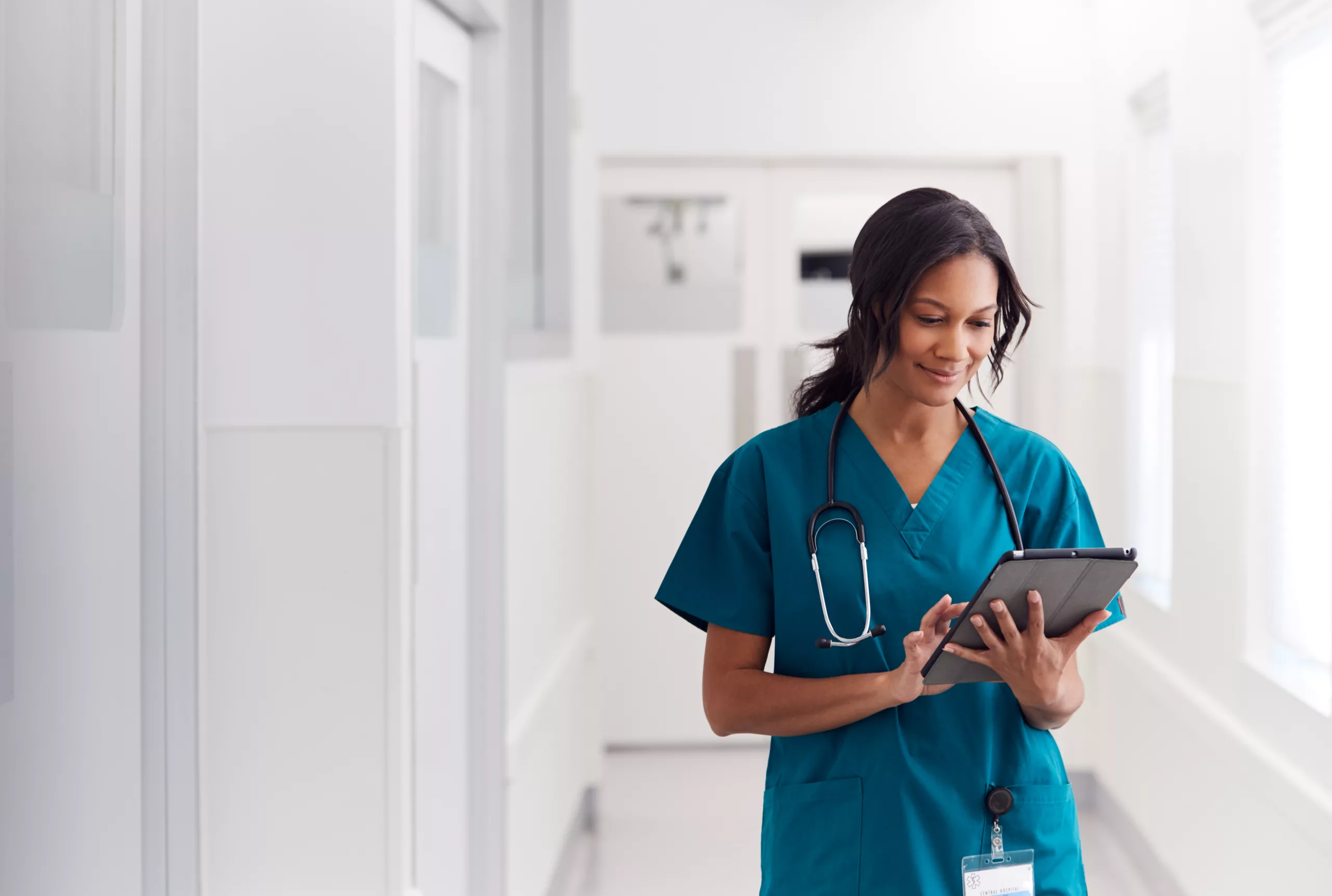 Female doctor wearing scrubs in hospital corridor using digital tablet working an in-demand healthcare job
