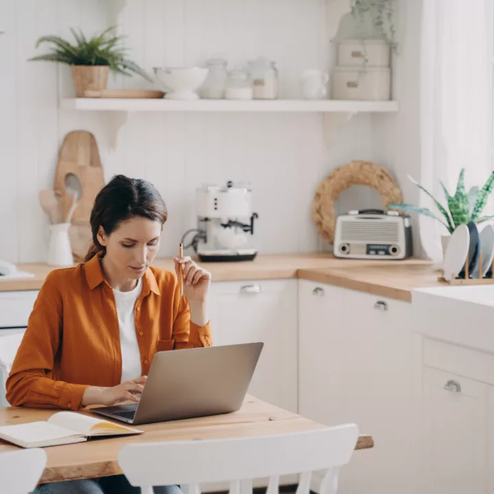 Female freelancer on her laptop next to a notepad at a table in her kitchen