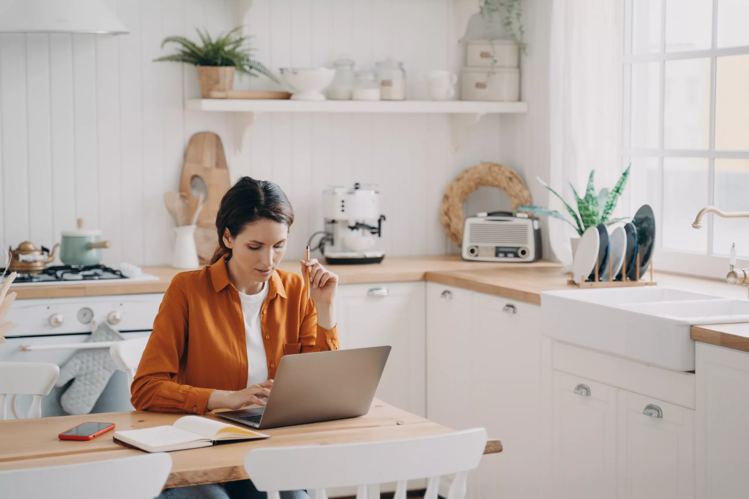 Female freelancer on her laptop next to a notepad at a table in her kitchen