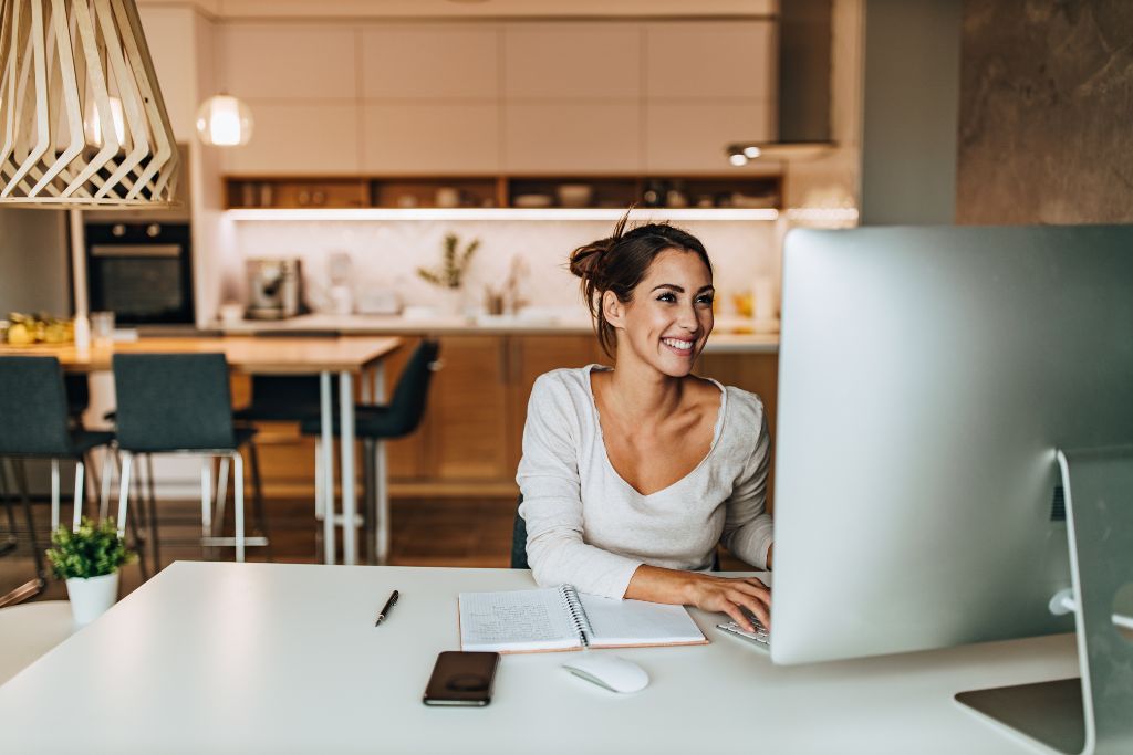 Smiling woman at home on her desktop computer searching for side hustles