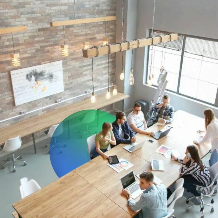 Employees gathered around large desk in a modern office with empty desks surrounding them due to a hiring freeze
