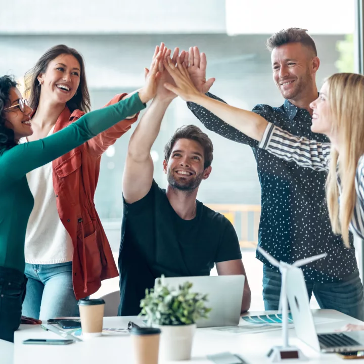 Business team celebrating a good job and encouraging each other while holding up their right hands around a desk in an office.