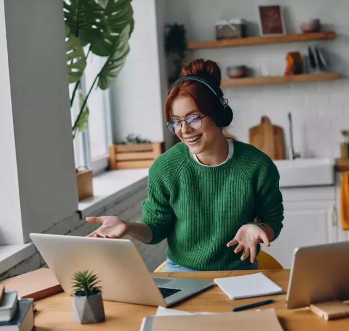 Cheerful young woman in headphones having web conference while working from home thinking about the future of remote work