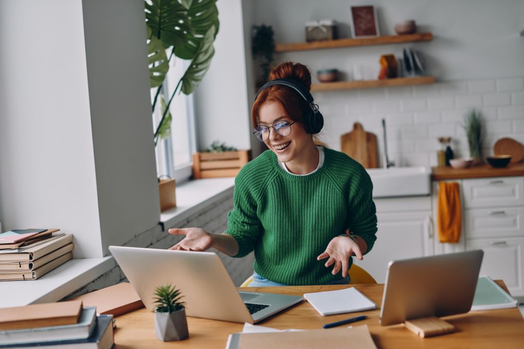 Cheerful young woman in headphones having web conference while working from home thinking about the future of remote work