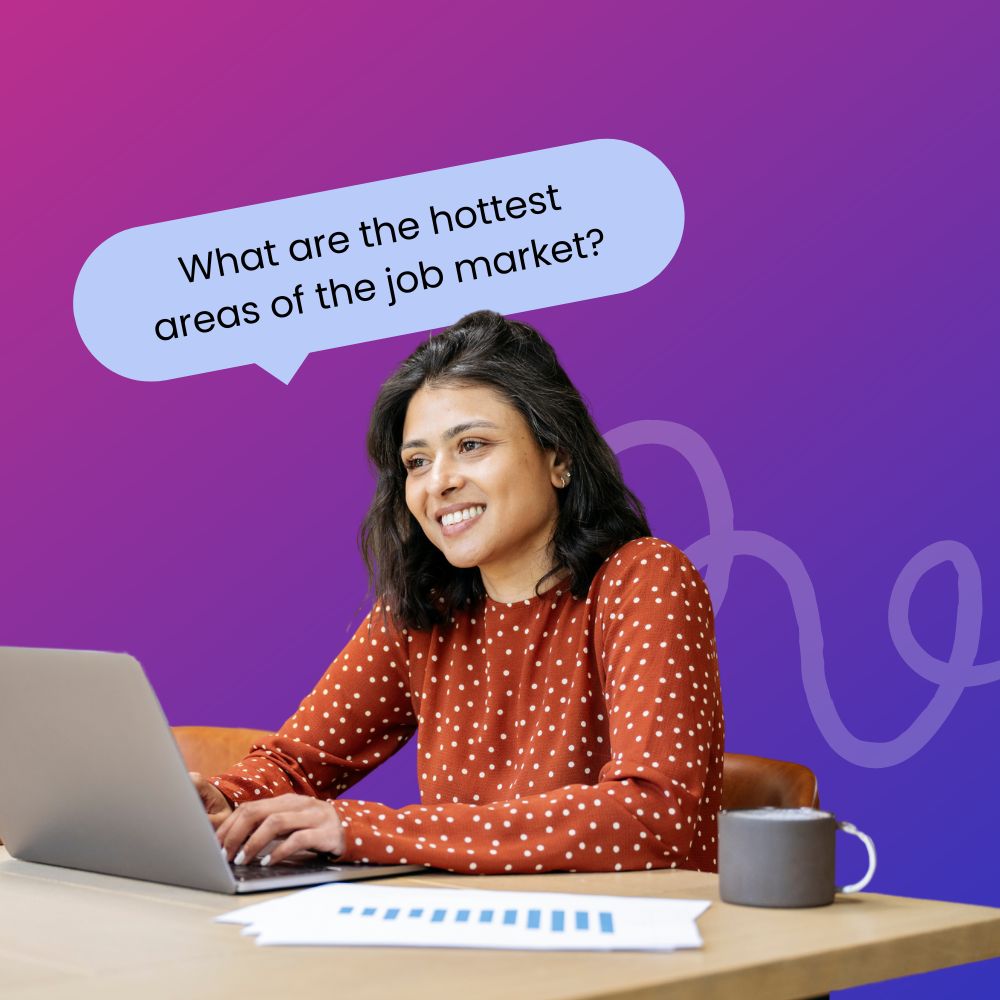 A smiling woman with dark hair wearing a red polka dot blouse is sitting at a desk, typing on a laptop. She is in a professional setting with a coffee mug and papers on the desk. Above her, a speech bubble asks, 'What are the hottest areas of the job market?'