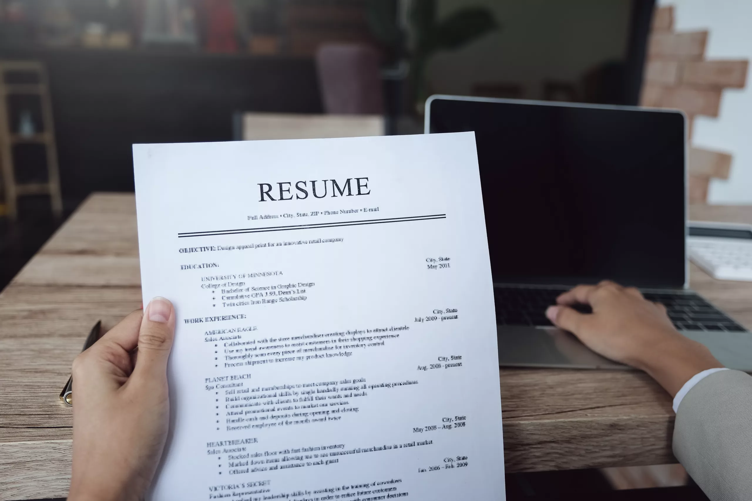 Professional holding their resume while using their laptop at a desk