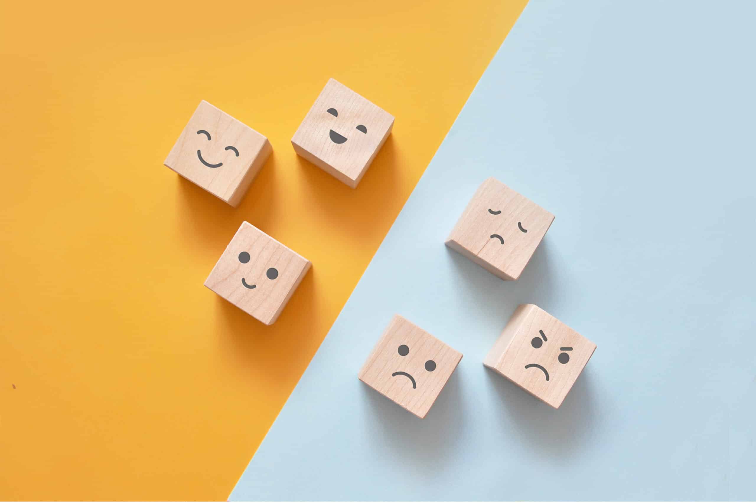 Wooden blocks with faces of different emotions separated by a diagonal line; emotional intelligence concept
