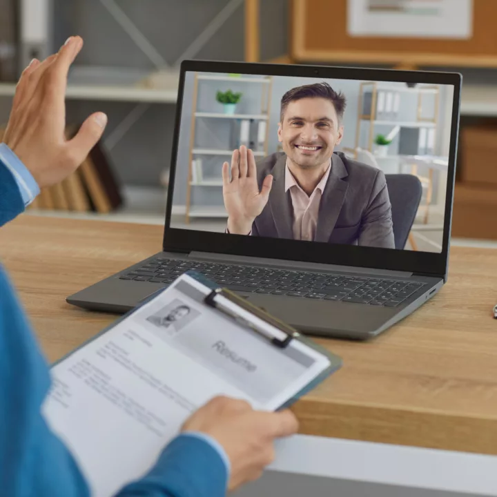 Smiling male recruiter with a clipboard greeting male job candidate during virtual online job interview