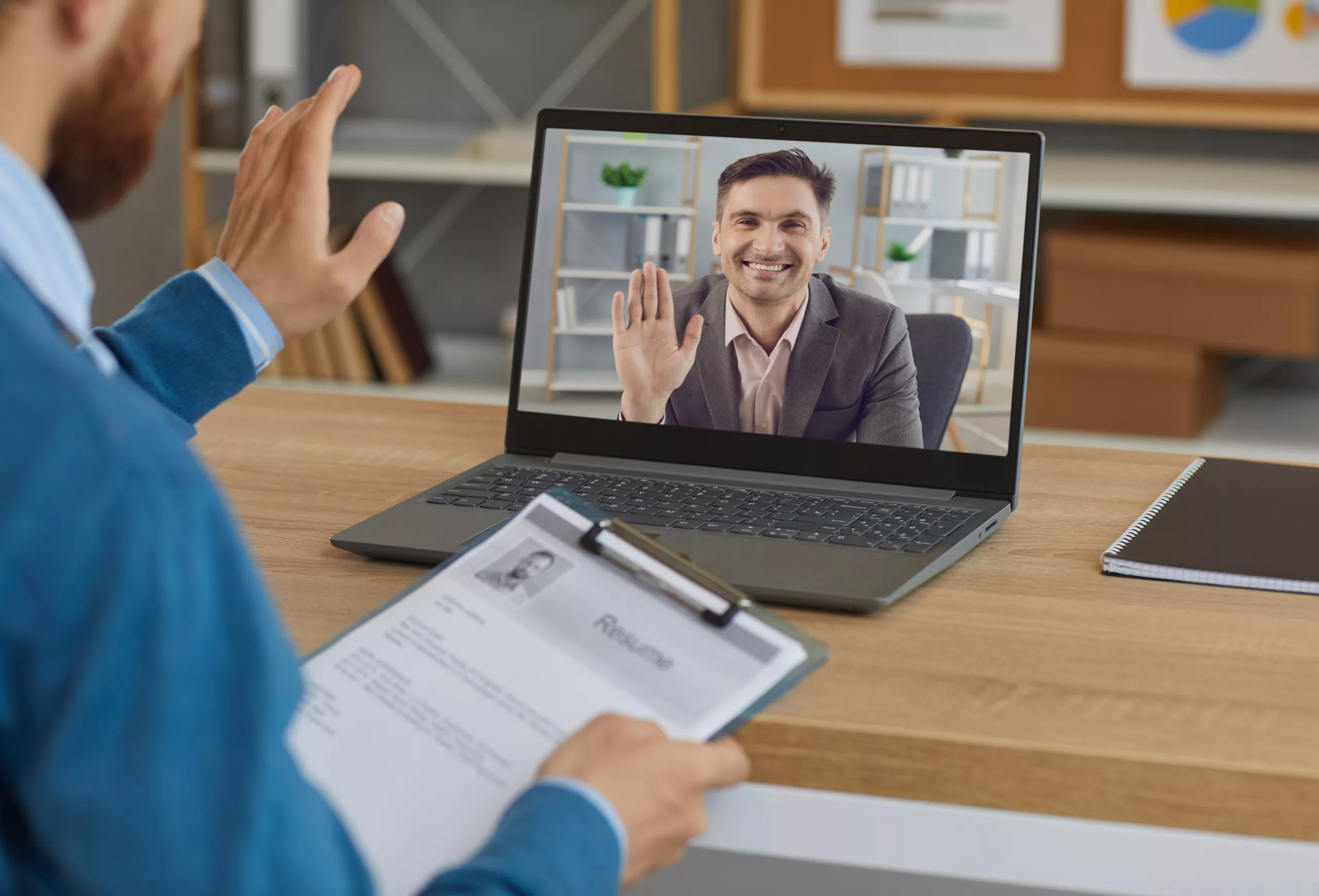 Smiling male recruiter with a clipboard greeting male job candidate during virtual online job interview