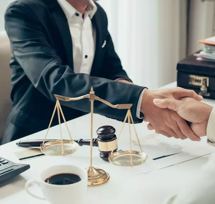 Businessman shaking hands to seal a deal with his partner lawyers or attorneys discussing a contract agreement sitting at a white desk with gavel.