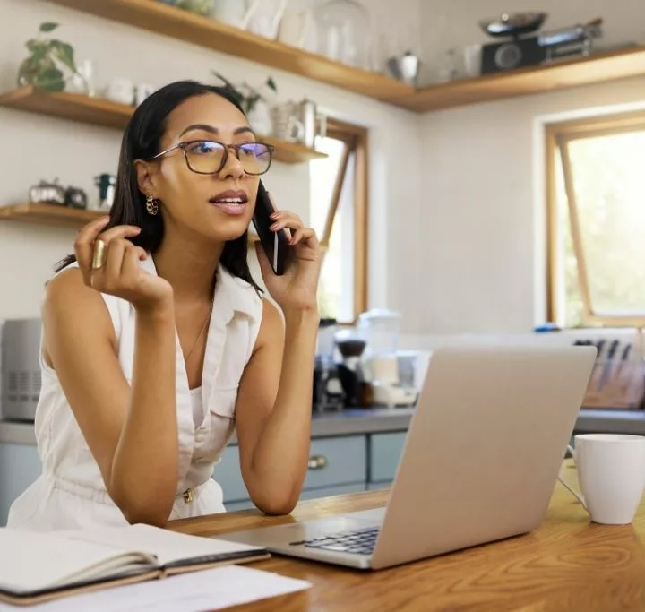 Woman professional looking distressed on the phone with her boss calling out of work in her kitchen sitting behind her laptop