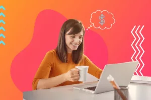 Young entry-level female professional wearing an orange long sleeve shirt holding a white mug sitting at a white desk behind a laptop at an office with a money symbol in a thought bubble