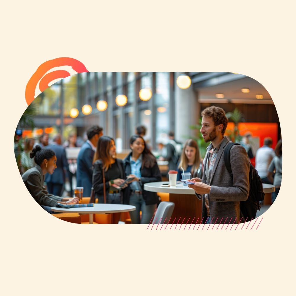 A young professional with a backpack stands at a table, looking thoughtful during a bustling networking event, highlighting the experience of an introvert in a social recruitment setting.